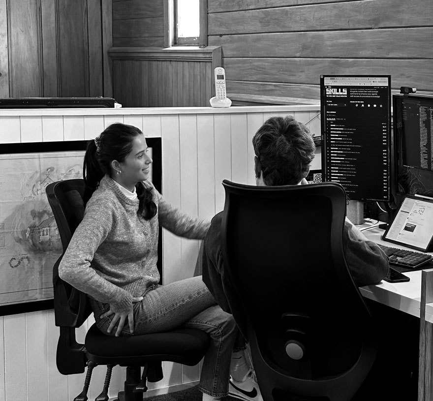 Two of the Wild team talking at a desk in the wood-panelled Wellington studio
